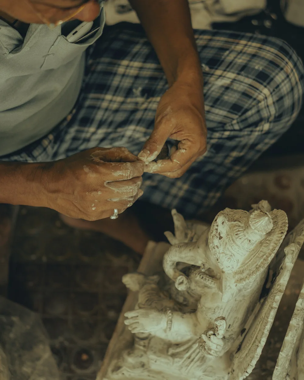 Cantero con mascarilla trabajando una figura de piedra con puntero y maceta en el taller